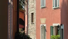 a row of brick and pink buildings, with windows and shutters, a palm tree, and a brick paved pathway