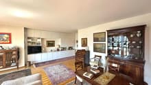 large living room with wooden dining table, 2 sofas, wooden chairs, white cupboards, wooden desk, glass cabinet, decorative items, framed pictures, carpet