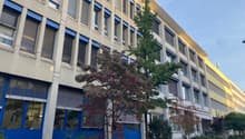 A multi-story building with blue window frames and a yellow wall, surrounded by trees and bushes.