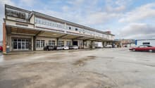 Industrial building with multiple windows, large parking area, cars parked in front, sign reading 'FLYING SUPPORTER IT BUSINESS SOLUTIONS'.