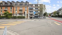 A multi-story building with balconies, a modern architectural design, and a street with traffic signs and bicycles parked in front.