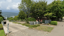 paved road, grassy area, metal fence, trees, building, mountains in the background