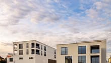 2 modern apartment buildings with balconies, multiple glass windows, elevated entrance