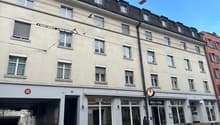 multistory building, large windows, ground floor commercial space, several people walking