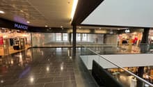 large shopping mall, empty, tiled floor, high ceiling, shops, sign for MANOR, light and glass railings