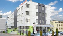 5 story building, large glass windows, green accents, garage entrance, cars parked in front