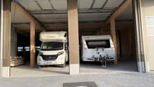 Two vehicles parked in a garage, one is a camper van and the other is a trailer.