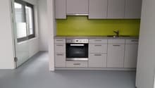 Modern kitchen with gray cabinets, green backsplash, built-in oven and dishwasher, and a sink with faucet