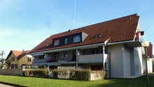 3 story residential building, brown roof, balconies on 2nd and 3rd floor, fence, grass