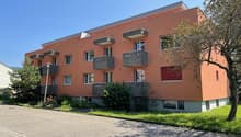 3-story apartment building, orange exterior, multiple balconies, windows, concrete base, greenery