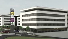 Modern office building with glass facade, multiple floors, parking area, trees, and a signboard with various logos