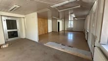 Empty room with tiled floor, white walls, wooden ceiling, and multiple windows.