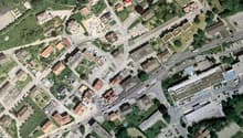 Aerial view of a town with multiple buildings, roads, and parking areas. The area is surrounded by trees and grass.