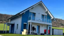 Two-story modern house with white exterior and blue accents, large windows, balcony, and attached garage.