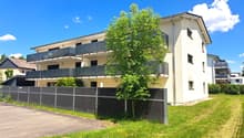 3-story apartment building with balconies, surrounded by green grass and trees