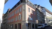 5-story building, red brick, white shutters, several windows, lamp on wall, multiple vans parked
