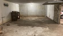 Empty parking area with concrete floor, brick wall, single car entrance, metal door, small window, car in front of garage.