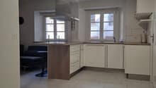 Modern kitchen with island, white cabinets, central island, sink with faucet, kitchen windows, tiled floor, overhead lighting.