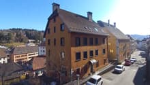 3 story house, brown roof, multiple windows, cars parked on street