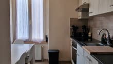 kitchen with dining area, white walls, wooden floor, white cabinets, white dining table, white chairs, white washing machine, dishwasher, white radiator, windows with white curtains, trash bin, ceiling lights