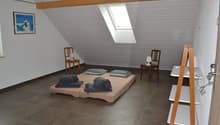 Attic bedroom with slanted ceiling, large window, hardwood floors, wooden beams, and a bed with gray bedding