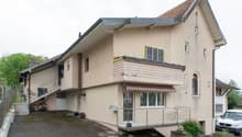 2-story house, beige exterior, brick base, staircase, balcony, awning, large driveway, plants, fence, parked car