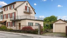 2 story house, beige exterior, red shutters, iron railing on balcony, wooden front door, garage at side, black gate