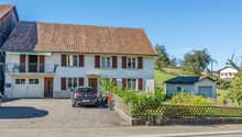 Two-story house, brown roof, large windows, balcony, garage, two cars parked in driveway
