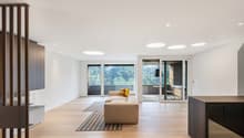 modern interior, white walls, hardwood floors, beige couch, decorative pillows, large windows with balcony, circular lights