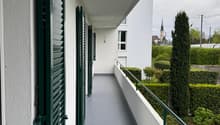 balcony with green shutters, gray floor, white walls, green railing, view of a garden