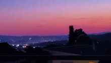 Sunset view from a balcony, cityscape, mountains, trees, and a clear sky