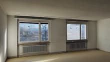 Empty room, with two windows, white walls, radiators, wooden floor, city view