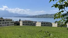 Wide field of grass, overlooking a large lake, multiple apartment buildings, mountains