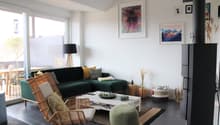 Living room with green sofa, coffee table, wooden chair, lamp, fireplace, and large windows