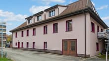 pink facade, brown roof, multiple windows, ground floor entrance, parking area, balcony