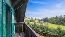Balcon en bois avec vue sur la campagne et les arbres verdoyants.