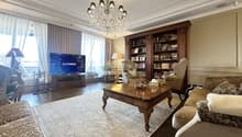 A large room with wooden flooring and furniture, chandelier, bookcase, couch, TV, table, chairs, and rugs.