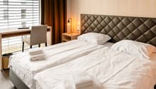 Spacious bedroom with large windows, quilted headboard, bedside tables, and a desk area
