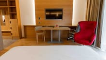 A bedroom with a large bed, a desk, a TV, and a chair.