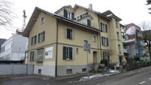 Yellow facade building, several floors, balconies, windows with shutters, sign with 'Siegel' on the wall, bicycles parked on the sidewalk