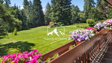 wooden balcony, lush lawn, purple and pink flowers, green trees, mountains