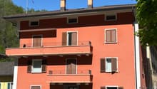 3-story apartment building with a red exterior, balconies on each floor, and chimneys on the roof.