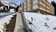 Modern wooden and stone building, multiple balconies, multiple levels, snow-covered hill
