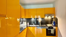 modern kitchen with yellow cabinets, wooden floor, stainless steel appliances, black countertops
