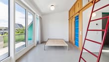 Empty room with a bed, large windows, balcony, wooden ladder, wooden cabinets, white walls, ceiling lamp