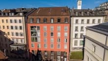 5 story building, red and white facade, many windows, balconies, green roof