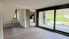 Spacious open-plan living area with large windows overlooking a balcony or terrace, hardwood flooring, and a staircase leading to another level.