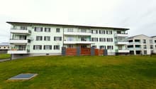 3 story apartment building, green exterior, multiple balconies, large grassy area in front