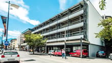 multi-story building, white exterior, multiple windows, cars parked in front, street with cars and pedestrians