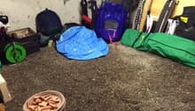 The image shows a cluttered garage space with various items such as tools, equipment, and storage containers scattered around the floor.